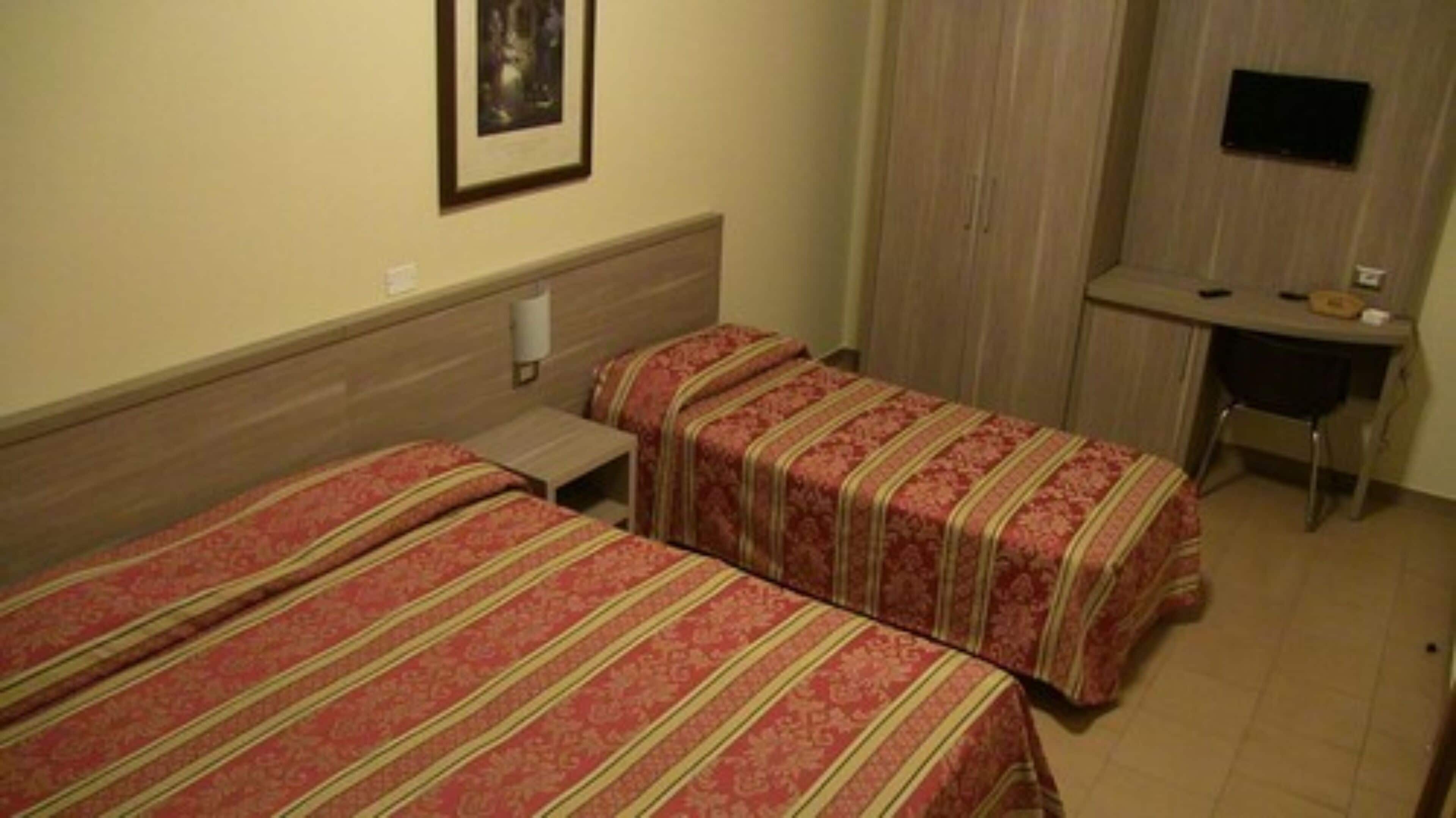 Une chambre d’hôtel avec deux lits simples, un bureau et un téléviseur fixé au mur.