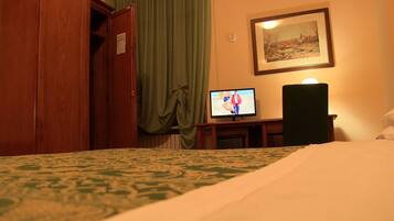 Habitación de hotel con cama, televisor sobre un soporte, un cuadro en la pared y una puerta.