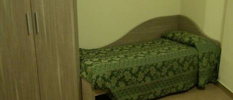 A small room with a single bed, a wardrobe, and a plain wall.