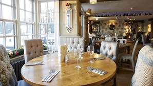 A dining area with round wooden tables, upholstered chairs, and a fireplace in the background. - Two Brewers by Chef and Brewer Collection (Kings Langley)