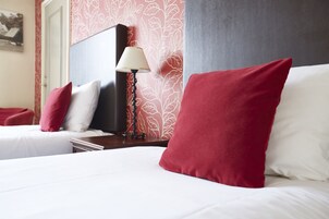 Habitación de hotel con dos camas, una mesita de noche, una lámpara y una pared con estampado floral.