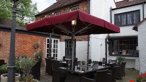An outdoor seating area with wicker furniture and a red umbrella. - Two Brewers by Chef and Brewer Collection (Kings Langley)