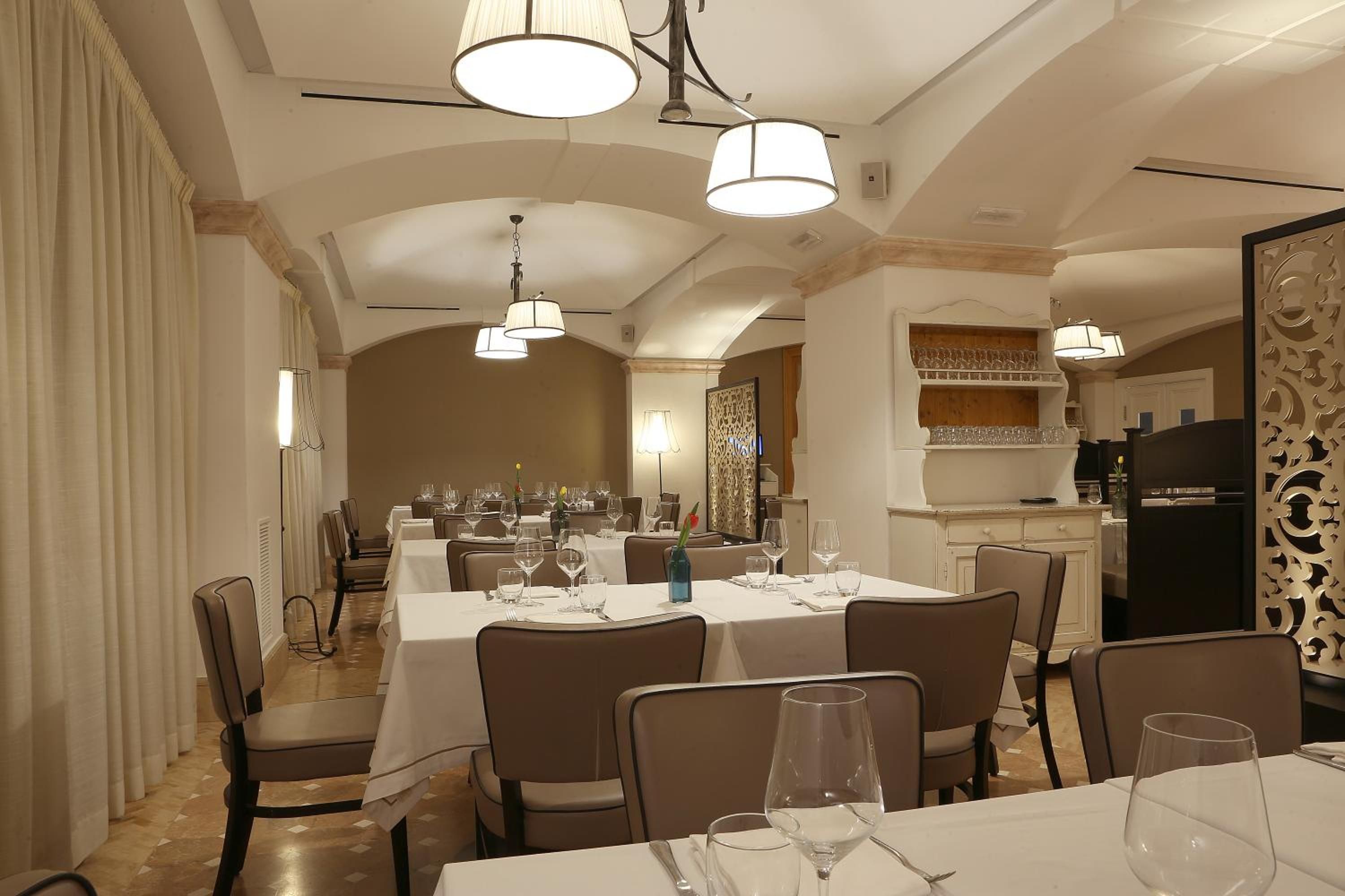 Un comedor con mesas dispuestas para una comida, sillas y lámparas colgantes.