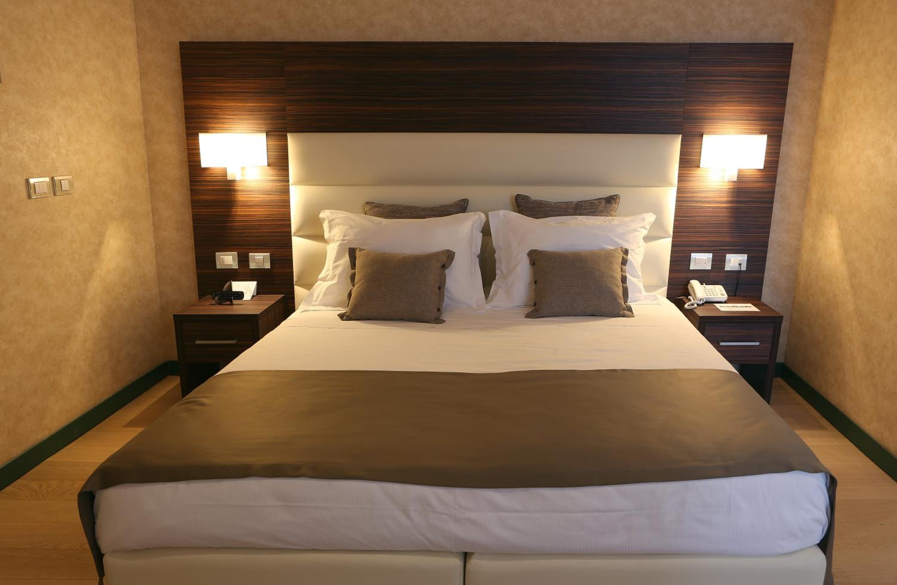 Habitación de hotel con una cama grande, dos mesitas de noche, cabecero con iluminación integrada y un teléfono en una de las mesitas.