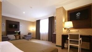 Habitación de hotel con cama, escritorio, silla, televisión y ventana con cortinas.