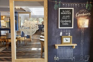 L’intérieur d’un restaurant présente un mur noir sur lequel est écrit un message accueillant, une photo encadrée et une enseigne indiquant « Goodwin’s Kitchen ».