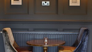 Een kamer met een ronde tafel, twee gestoffeerde stoelen en drie ingelijste kunstwerken aan de wand.