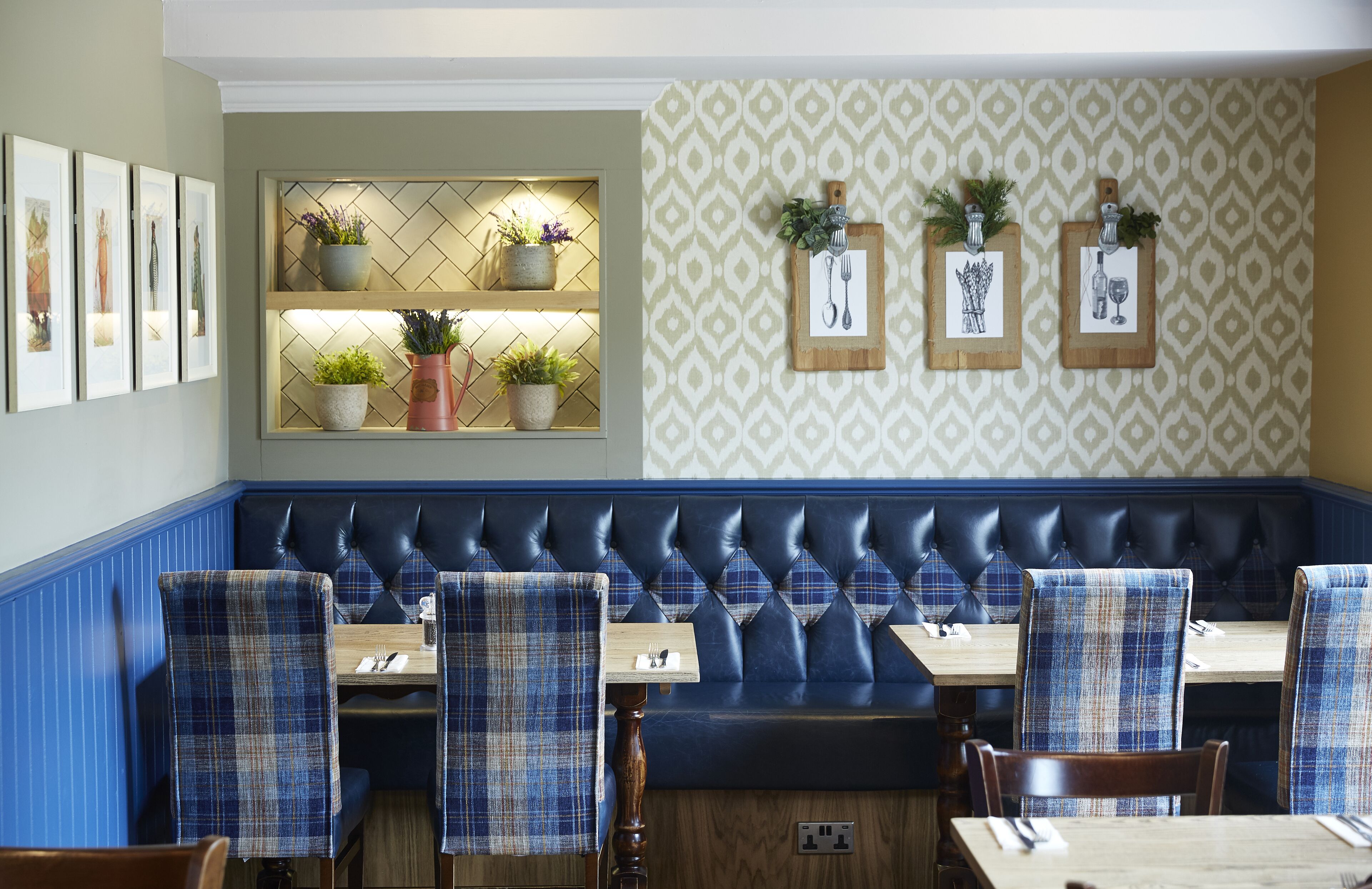 A restaurant with a blue upholstered booth seating area, wooden tables, and plaid-patterned chairs.