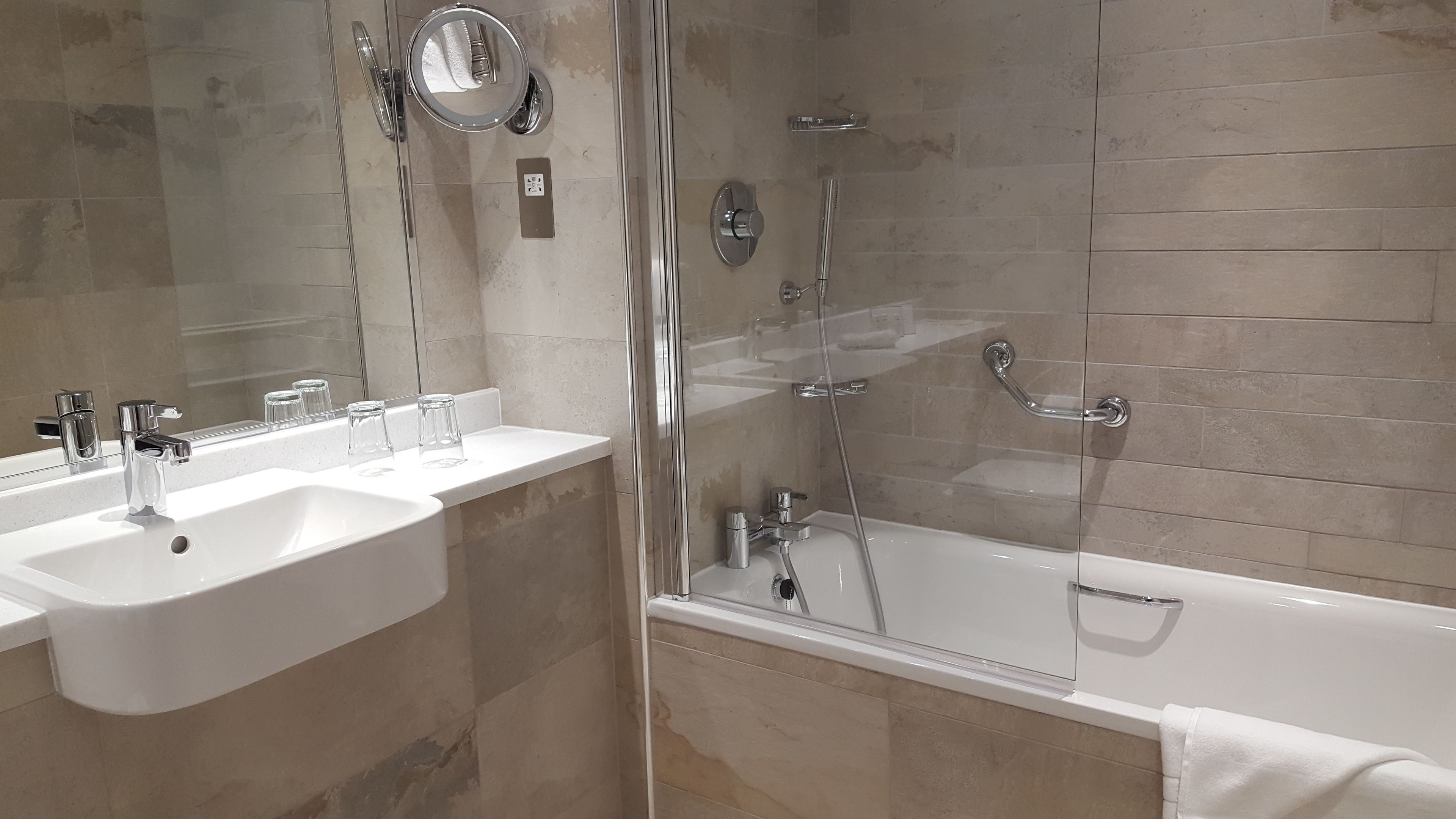 A modern bathroom with a glass-enclosed shower, a white bathtub, and a vanity with a mirror and two sinks.
