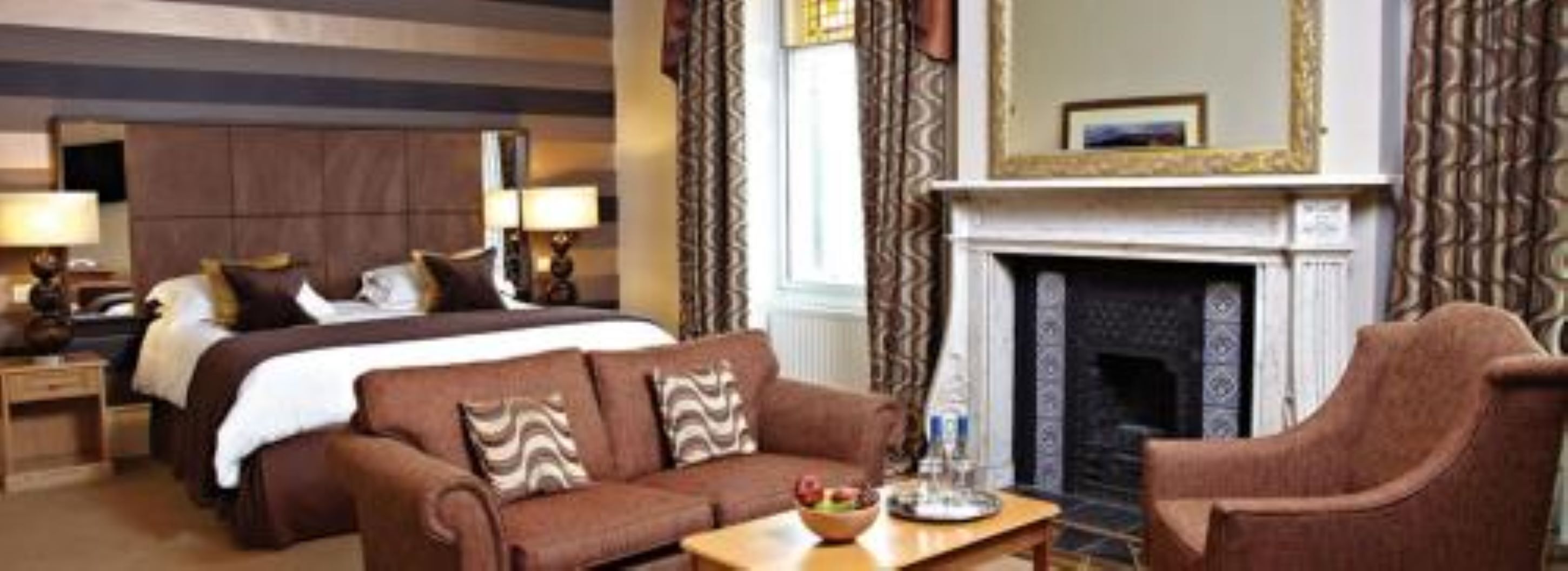 Une chambre d’hôtel avec un grand lit, un canapé, un fauteuil, une cheminée et un miroir.