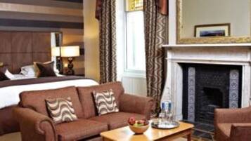 Une chambre d’hôtel avec un grand lit, un canapé, un fauteuil, une cheminée et un miroir.