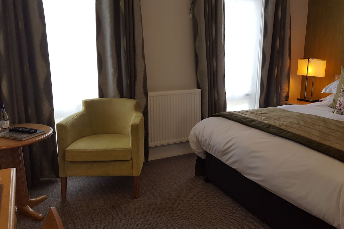 A hotel room with a bed, a chair, a small table, and a lamp.