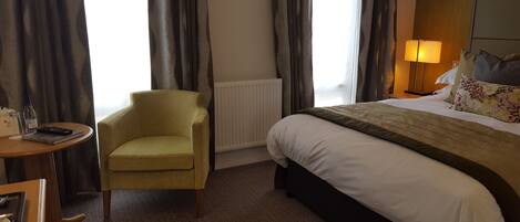 Une chambre d’hôtel avec un lit, une chaise, une petite table et une lampe.