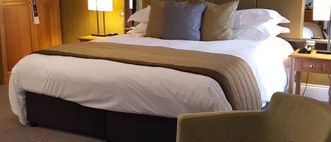 Une chambre d’hôtel avec un grand lit, un bureau avec une lampe, une chaise et une table de chevet avec une bouteille et des mouchoirs.