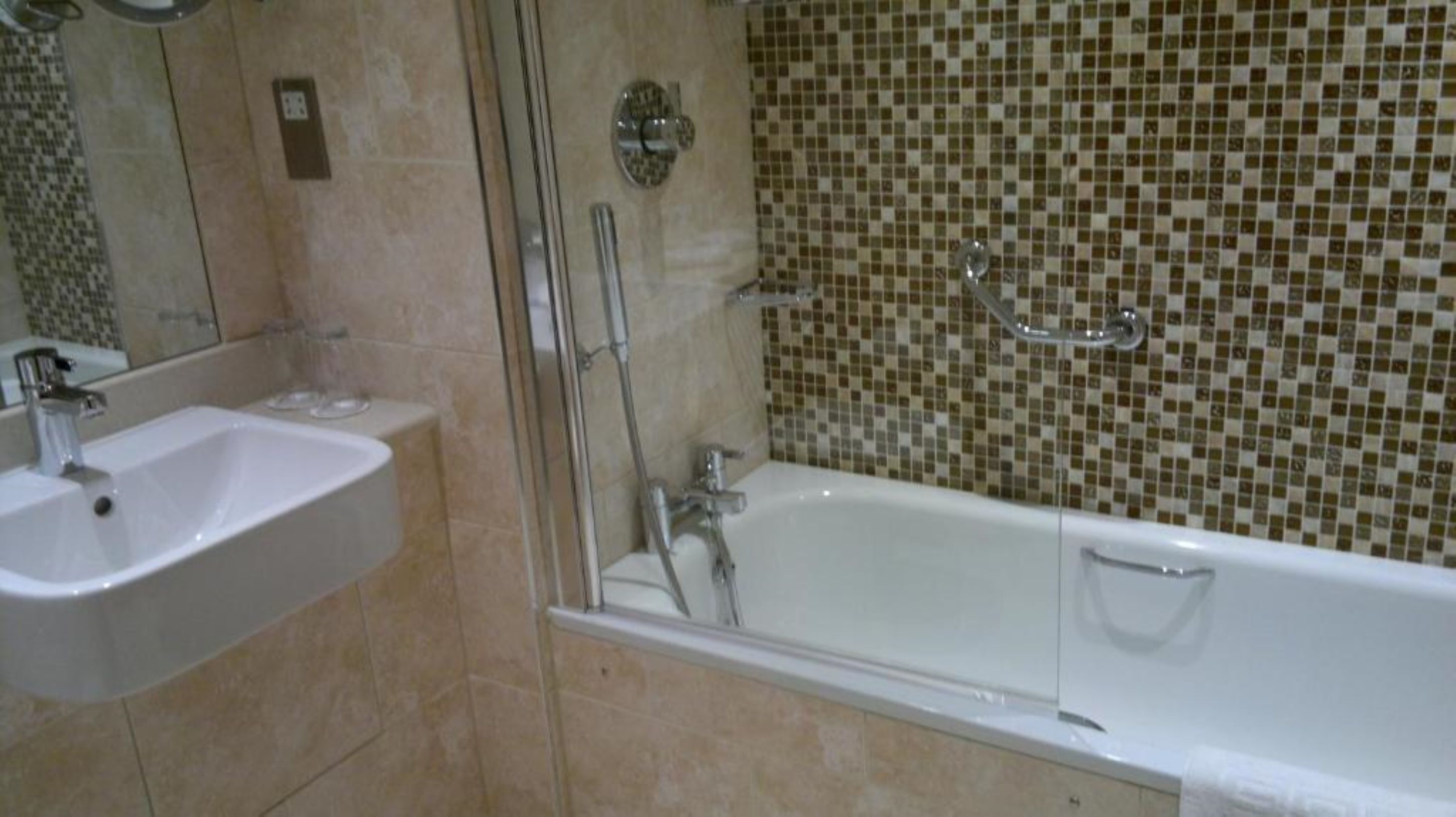 Une salle de bain avec un lavabo, un miroir, une douche et des murs carrelés.