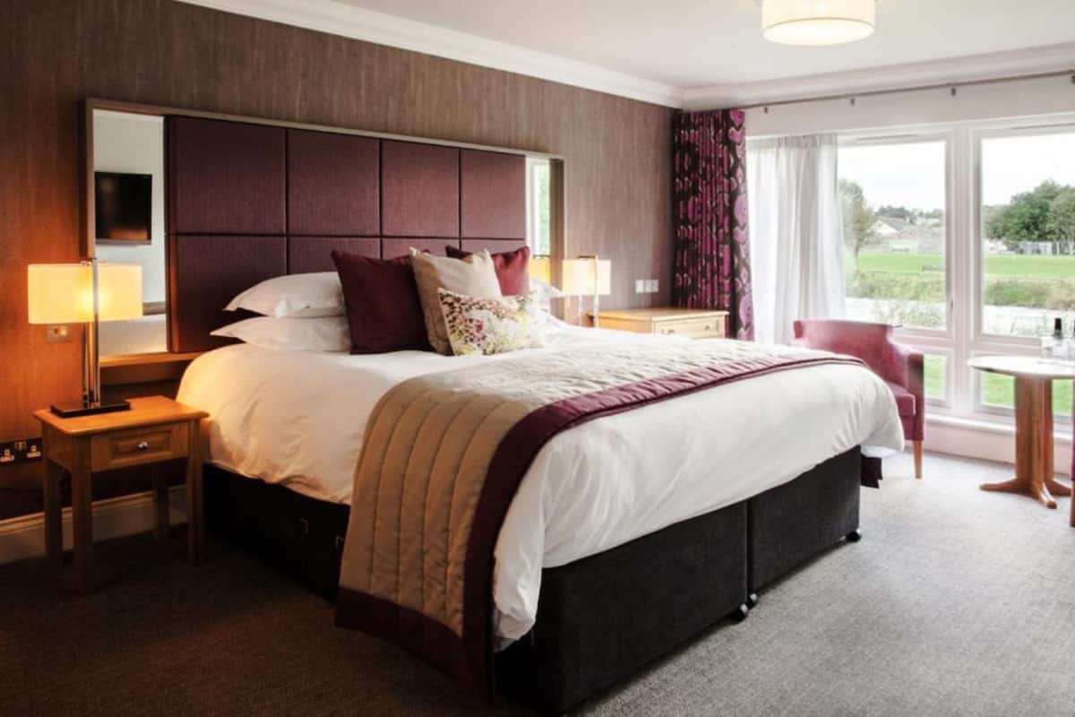 A hotel room with a large bed, two bedside tables with lamps, a small round table, and a chair.