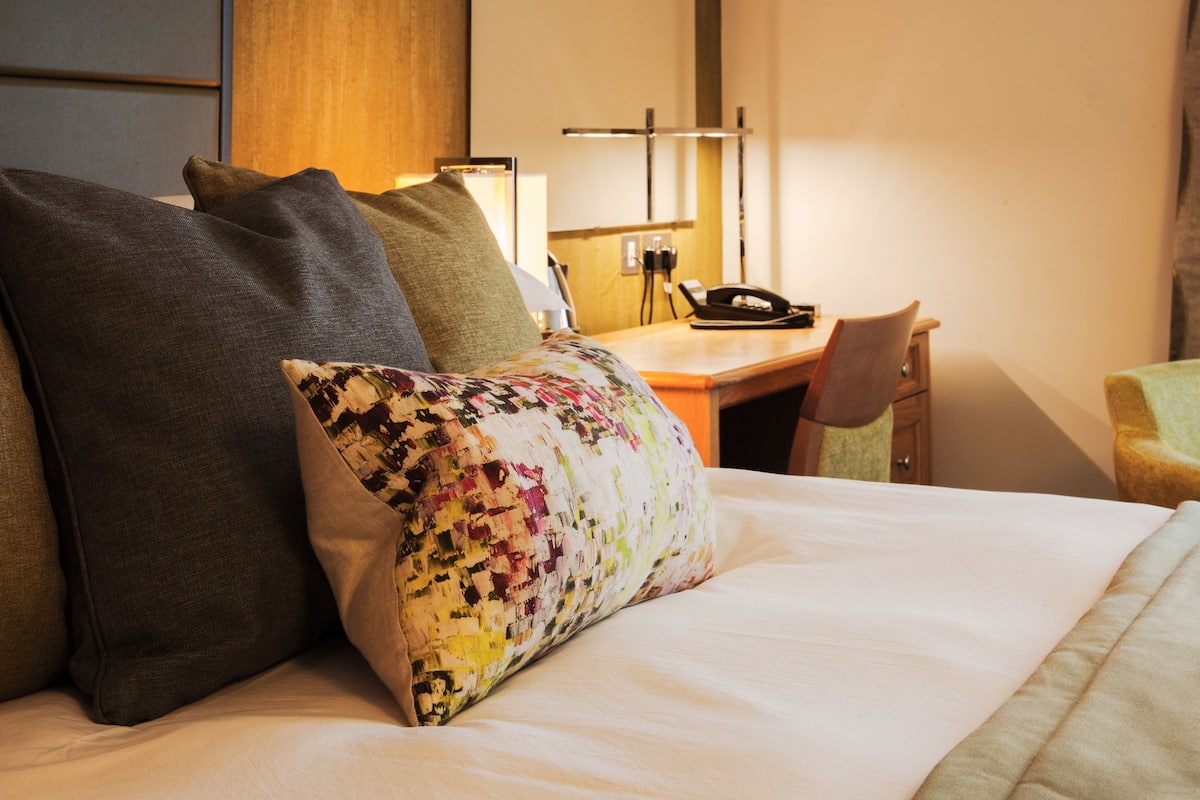 A hotel room with a bed, pillows, a desk with a telephone, and a chair.