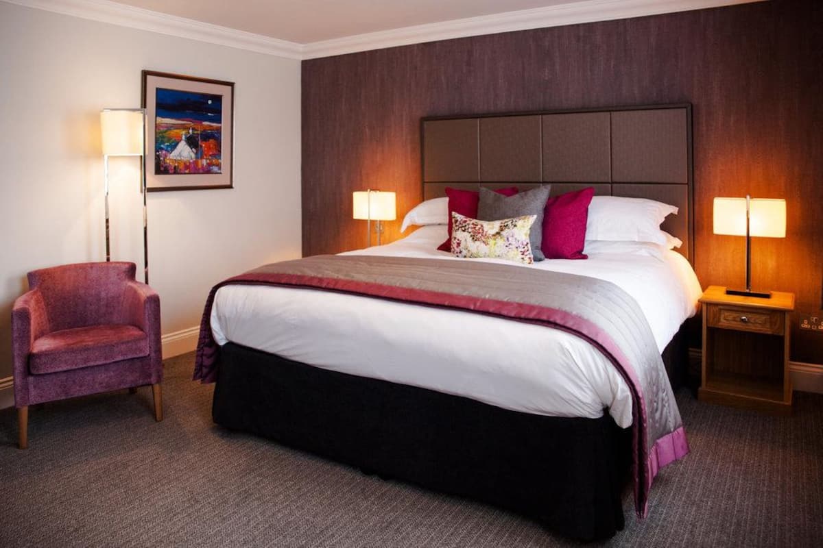 A hotel room with a large bed, two bedside lamps, a chair, and a framed painting on the wall.