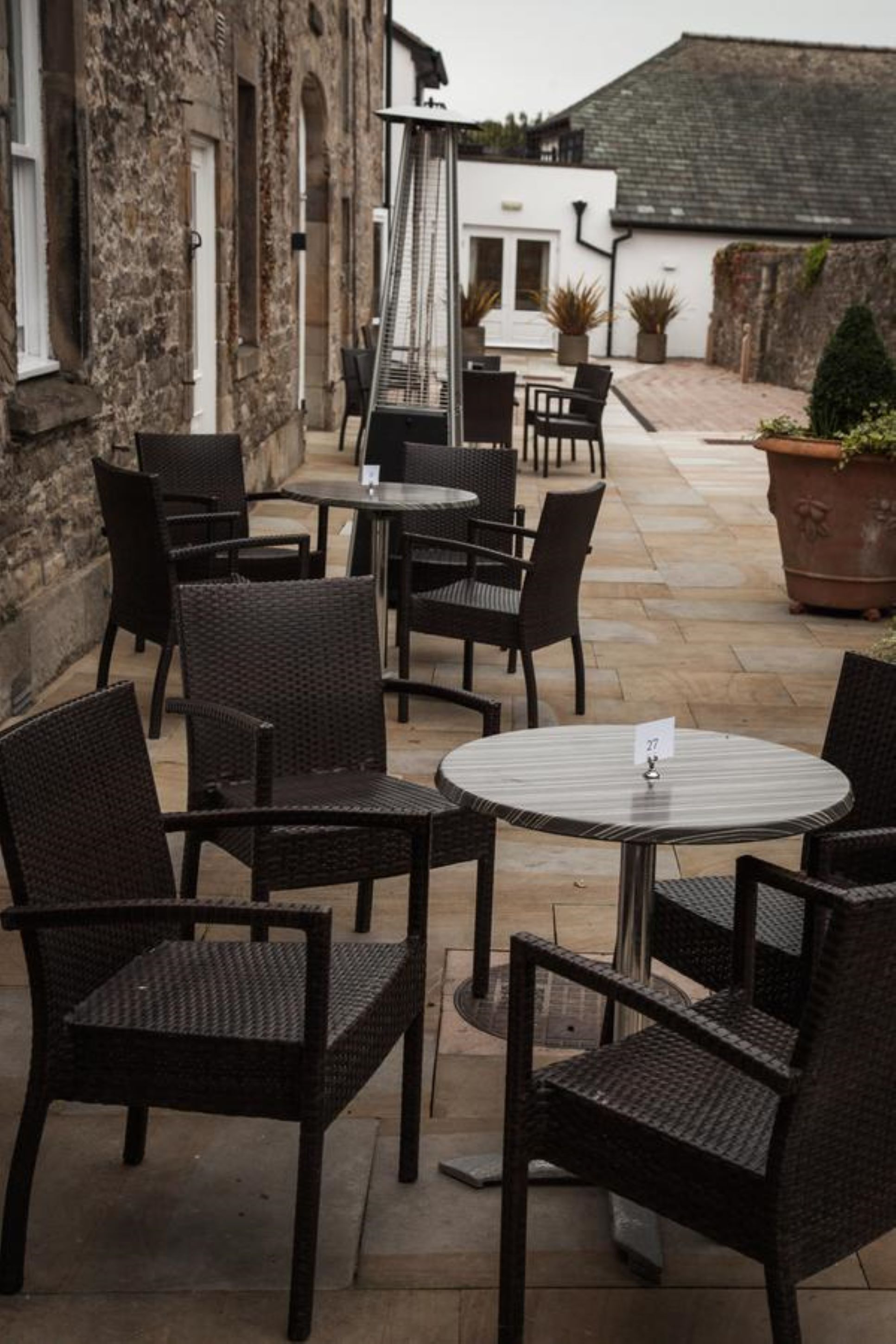Un espace extérieur aménagé en terrasse, avec des chaises et des tables en osier, des murs en pierre et des plantes en pot.
