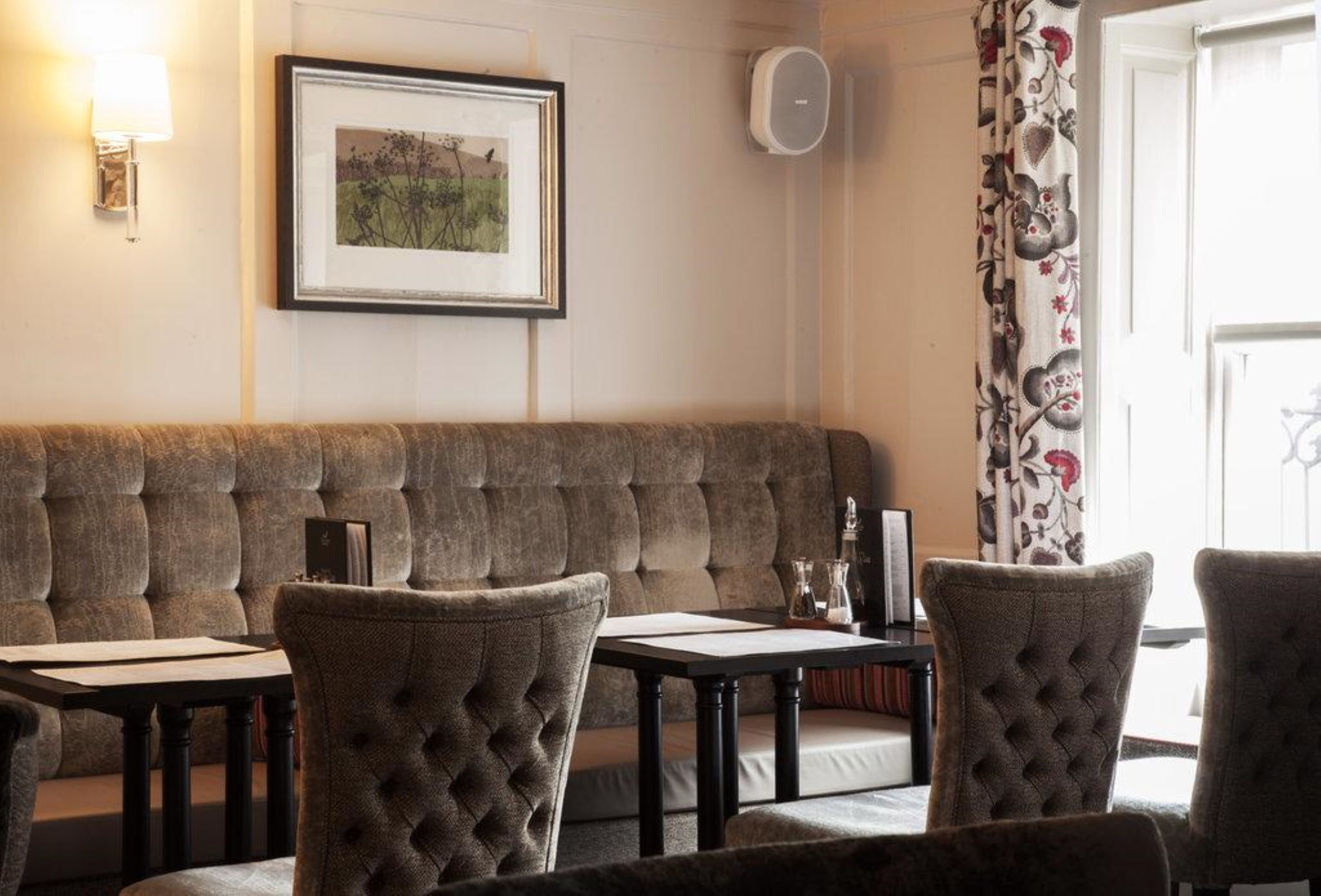 A cozy seating area with a cushioned bench and upholstered chairs, a framed picture on the wall, and a table with a lamp and a vase.