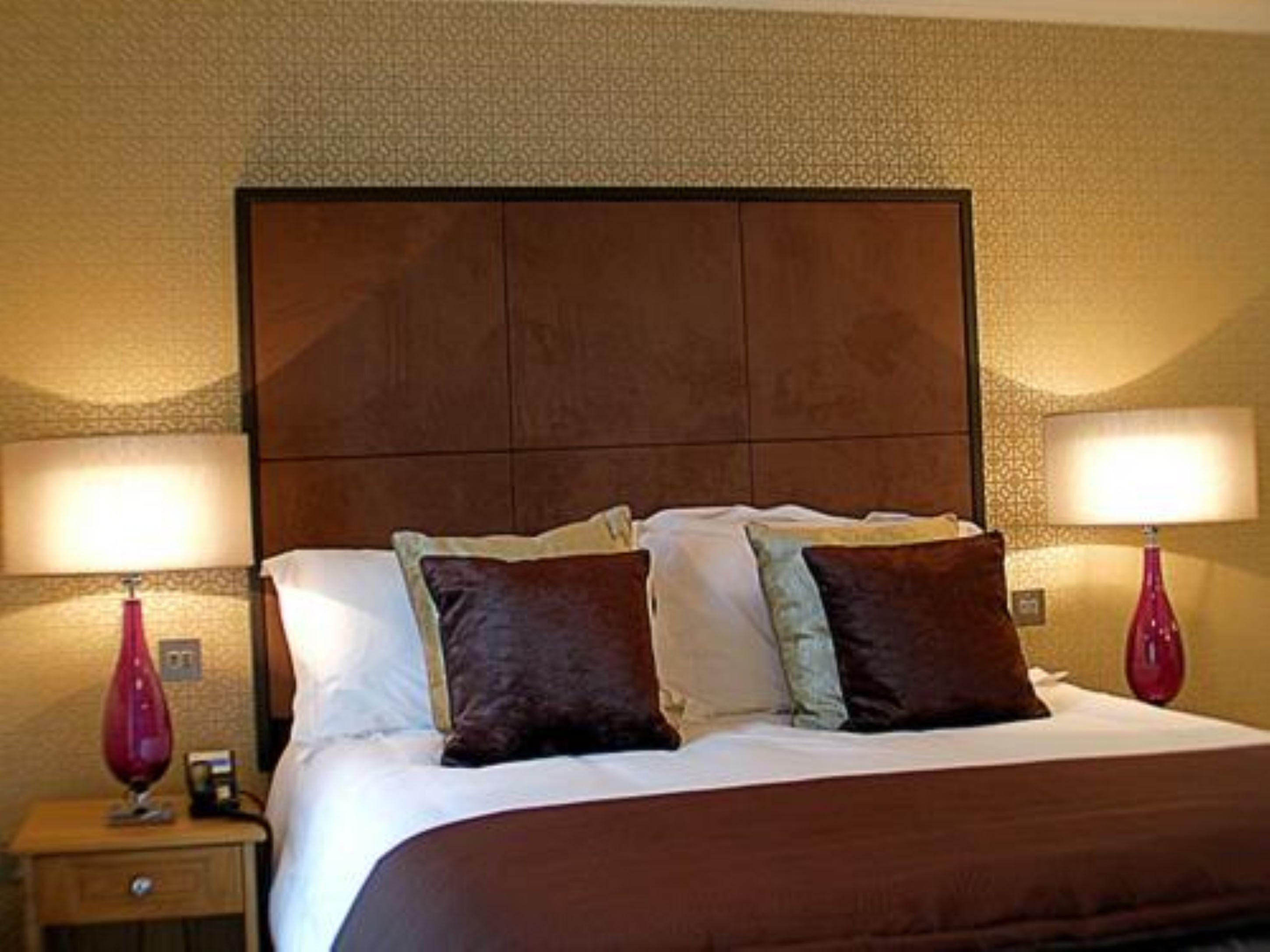 Una habitación de hotel con una cama grande, dos lámparas de noche y una mesita de noche con lámpara.