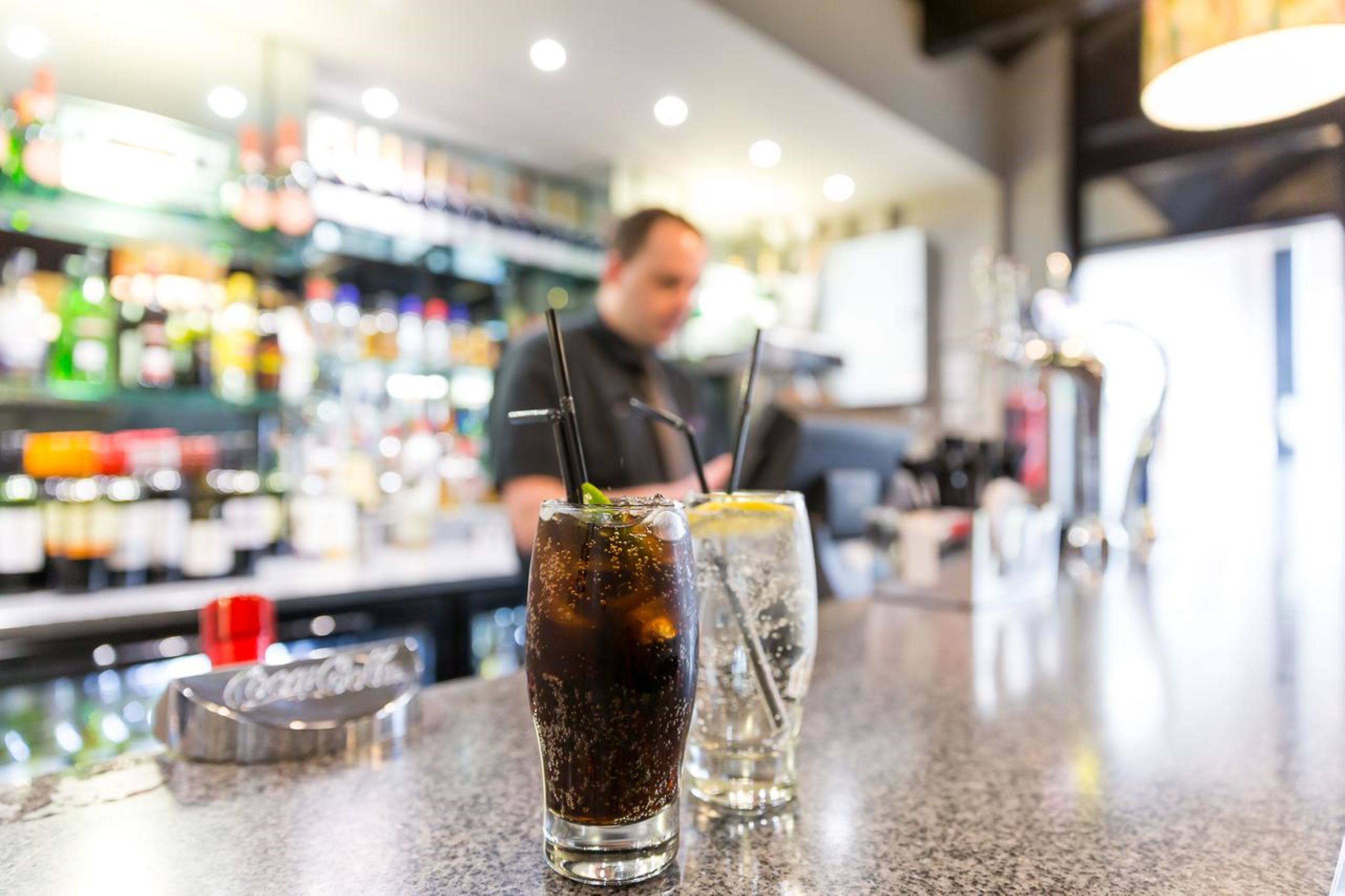 Una barra con dos bebidas, una oscura y otra transparente, y una botella de Coca-Cola.