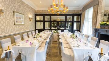 A formal dining room with long tables, white tablecloths, and silverware.