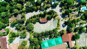 Vista aérea de una zona residencial con un camino circular central, rodeado de árboles y casas con tejados rojos.
