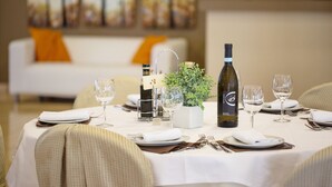 Mesa de comedor dispuesta con mantel blanco, copas de vino, una botella de vino y una pequeña planta en maceta.