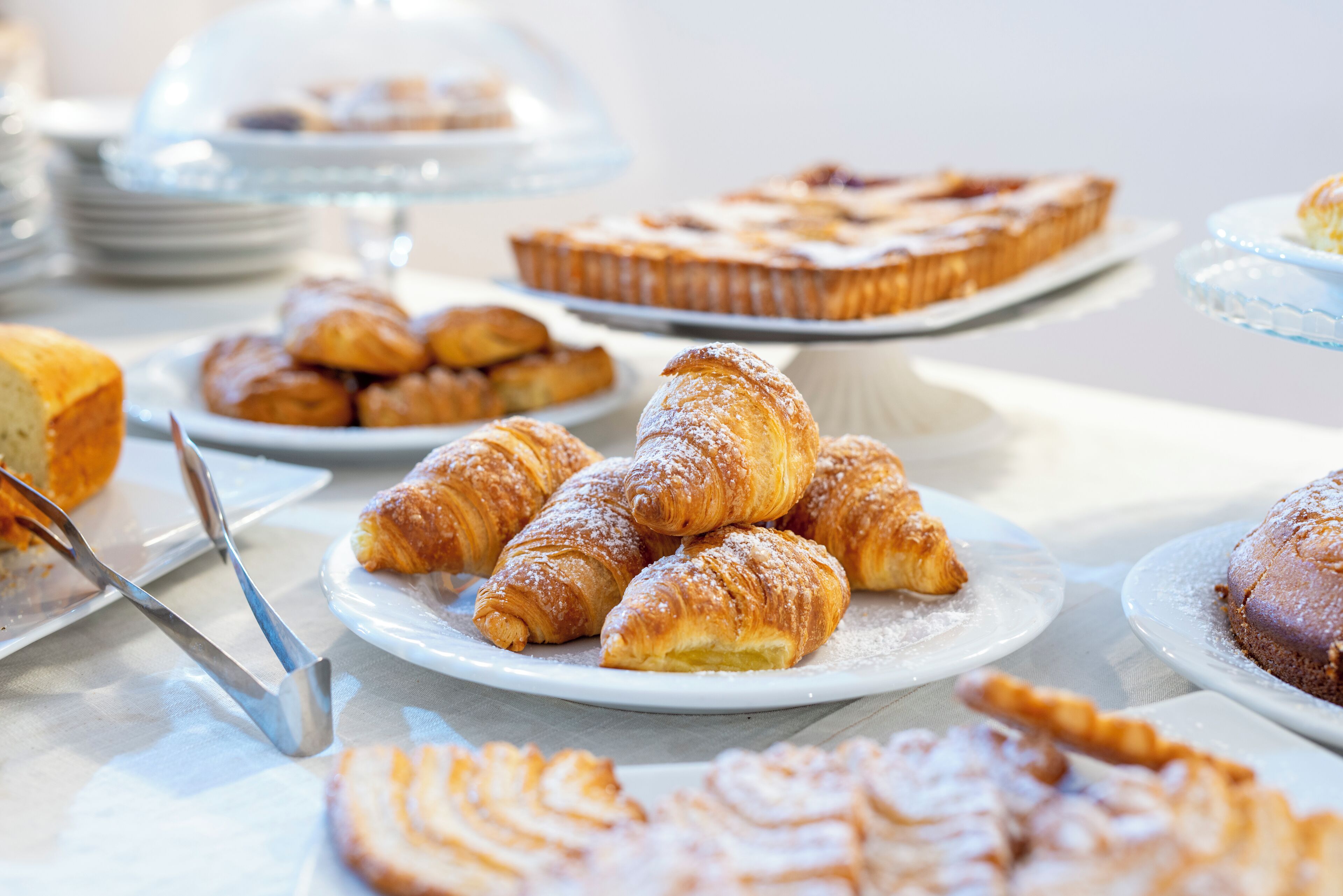Verschiedene Gebäcke und Desserts auf Tellern, darunter Croissants und ein Tarte, präsentiert auf einem Tisch.