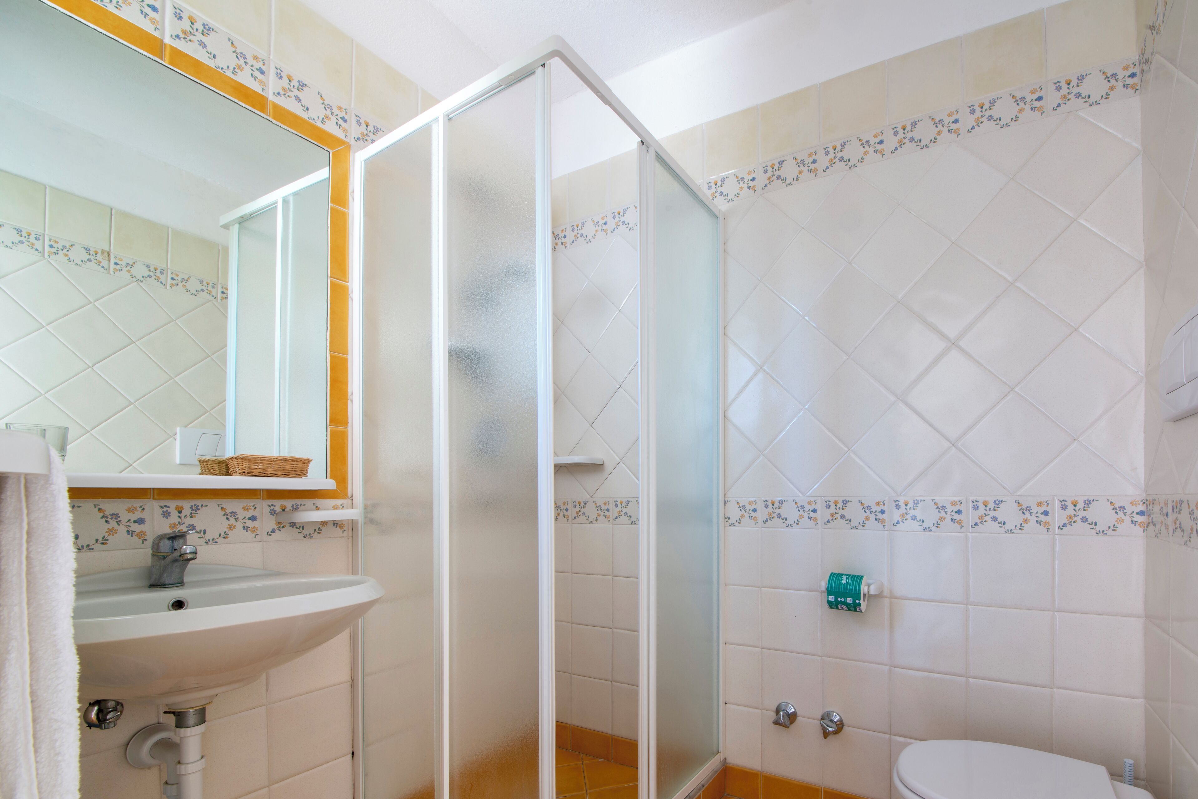 Un bagno con doccia vetro, lavandino, WC e specchio.