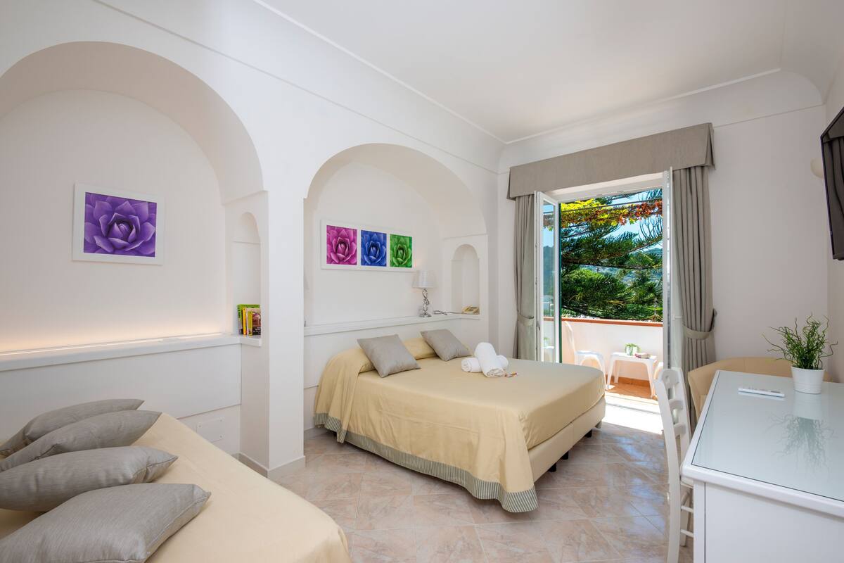 Habitación de hotel con cama, sofá, mesa y balcón con vistas a zonas verdes.