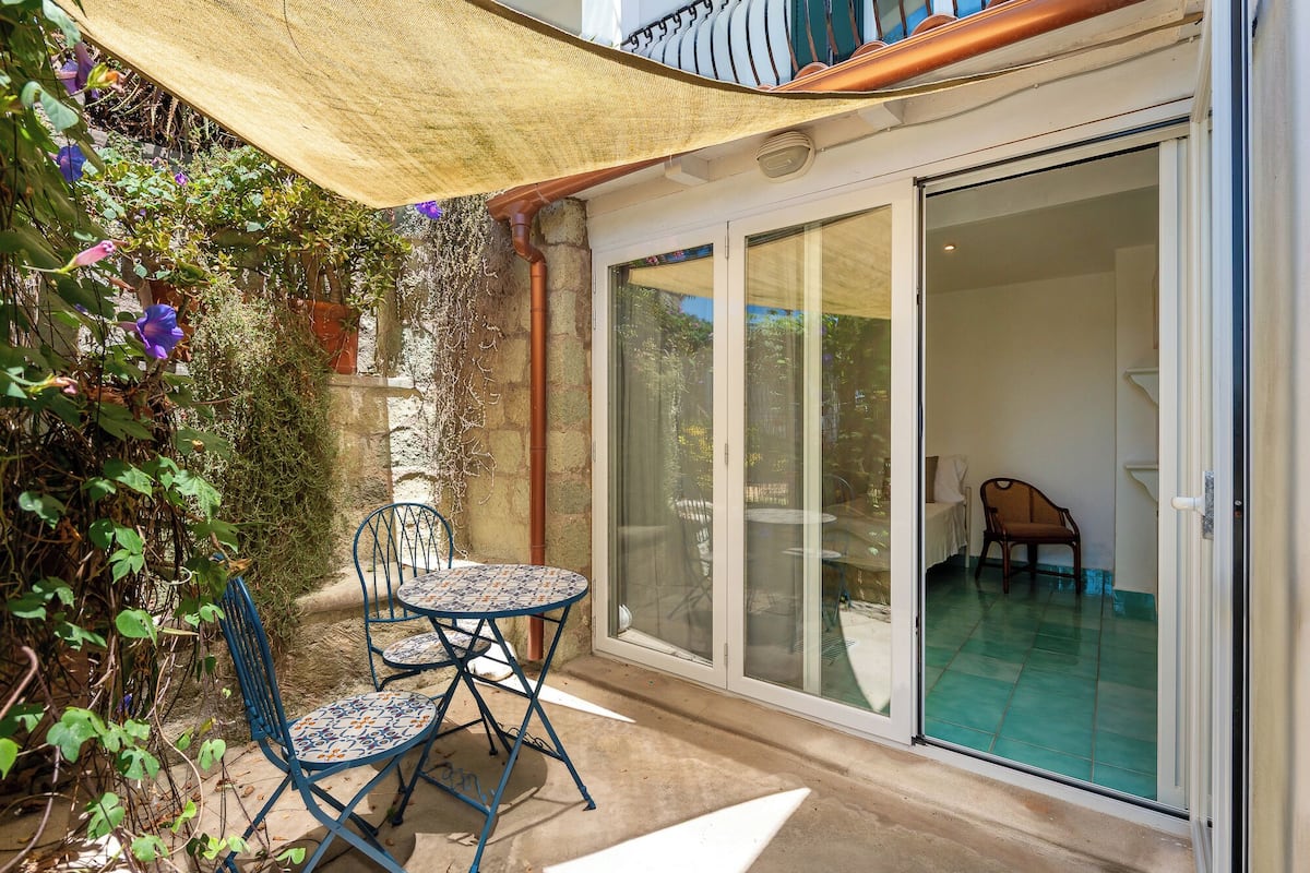 Un patio con una mesa y sillas, una puerta corrediza de vidrio que da a una zona de piscina y una pérgola que ofrece sombra.