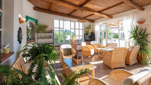 A spacious living area with wicker furniture, large windows, and potted plants. - Hotel Villa Melodie - Adults Only (Forio)