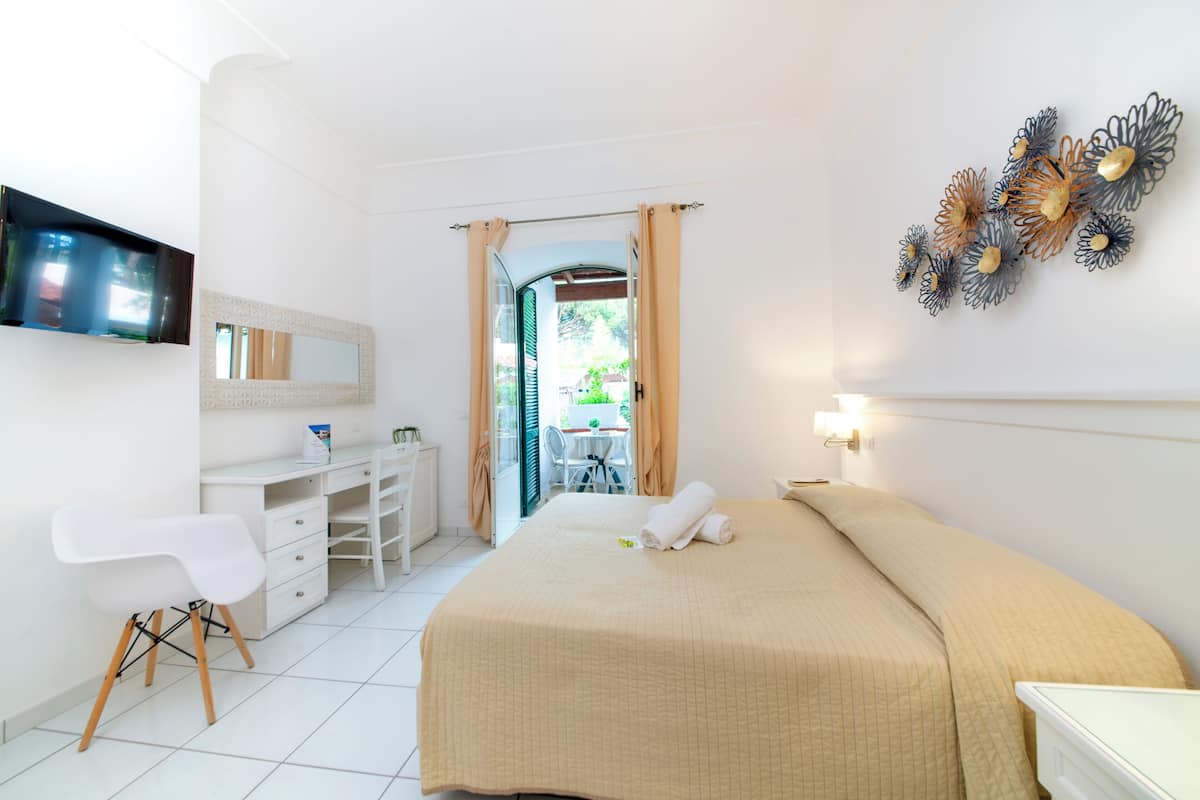 Habitación de hotel con cama, escritorio, silla, televisión y vistas al exterior.
