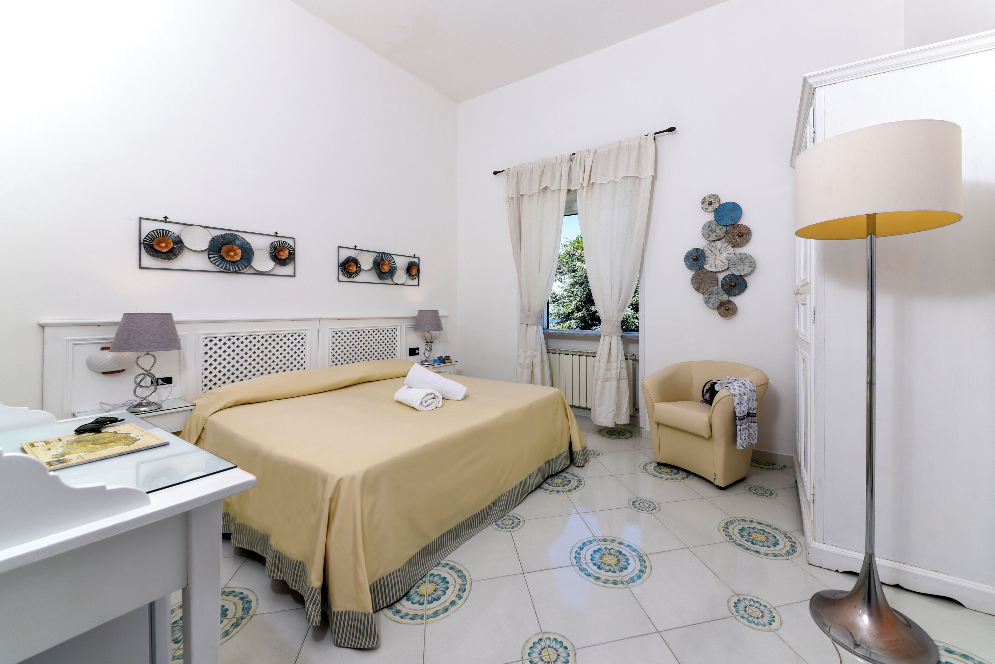 Habitación de hotel con cama, escritorio, silla, lámpara y decoración en la pared.