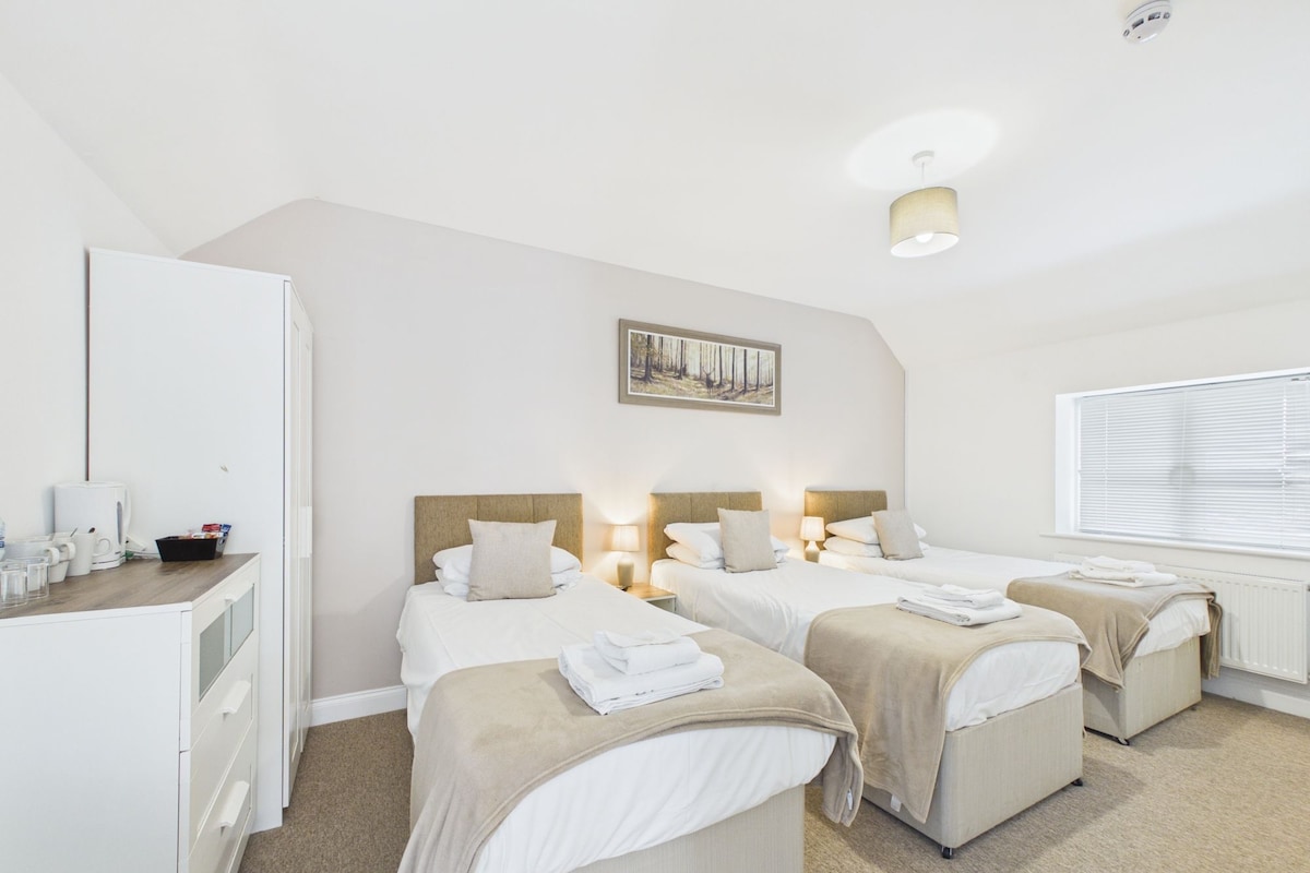 A hotel room with two beds, a desk, a chair, a radiator, and a window with blinds.
