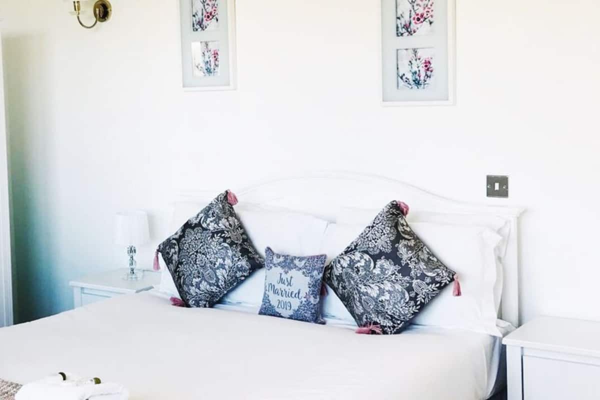 Una cama bien hecha con almohadas estampadas, una mesita de noche con lámpara y un armario con espejo.
