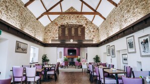 A spacious dining area with high ceilings and exposed stone walls, featuring a central fireplace and multiple dining tables and chairs. - Mendip Spring Golf Club (Bristol)