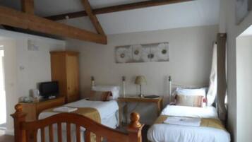 A room with two single beds, wooden headboards, a wooden wardrobe, a television, and a wall-mounted artwork.