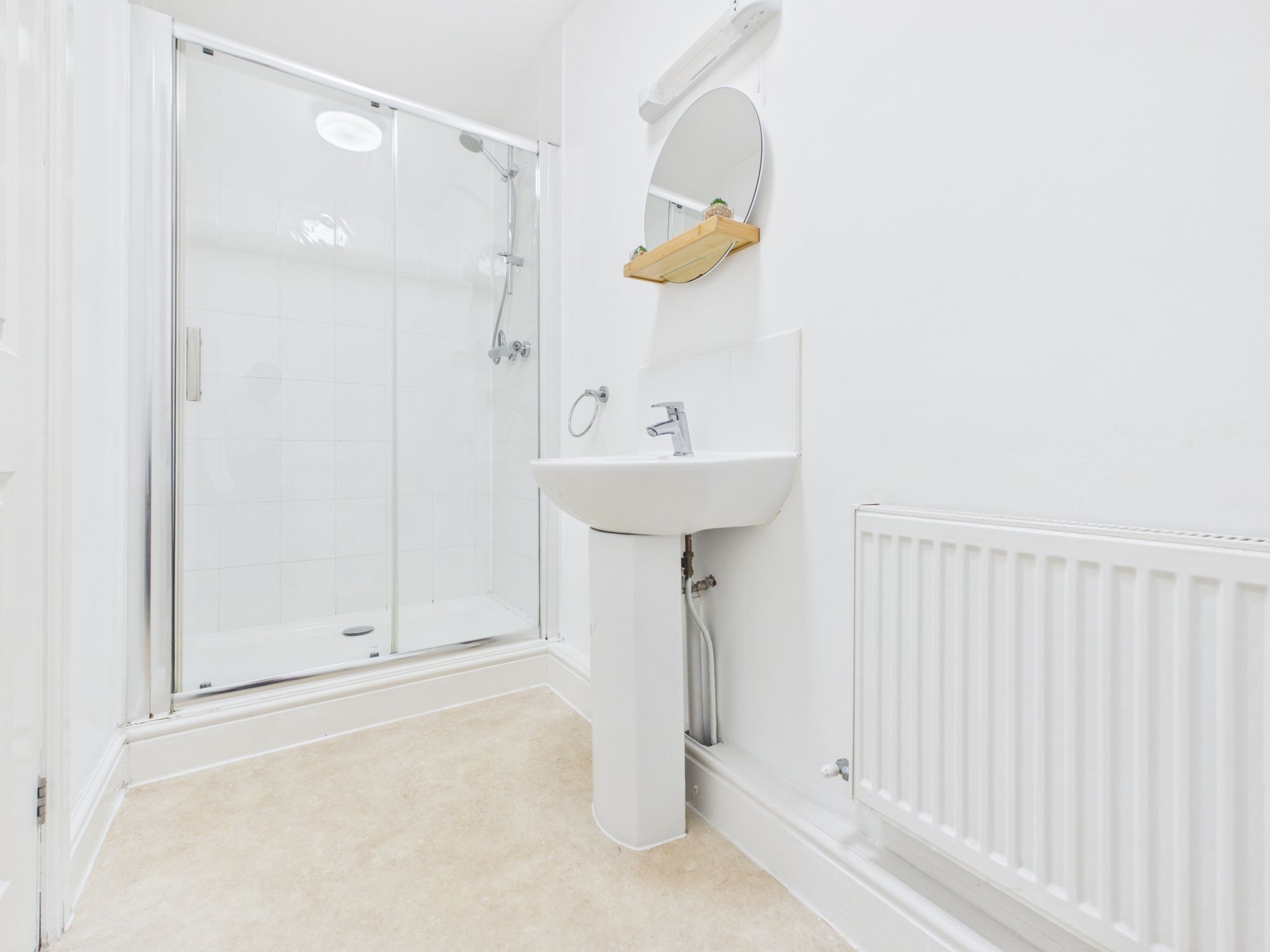 Un baño con cabina de ducha de vidrio, un lavabo blanco con espejo y un radiador en la pared.