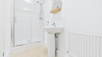 Un baño con cabina de ducha de vidrio, un lavabo blanco con espejo y un radiador en la pared.