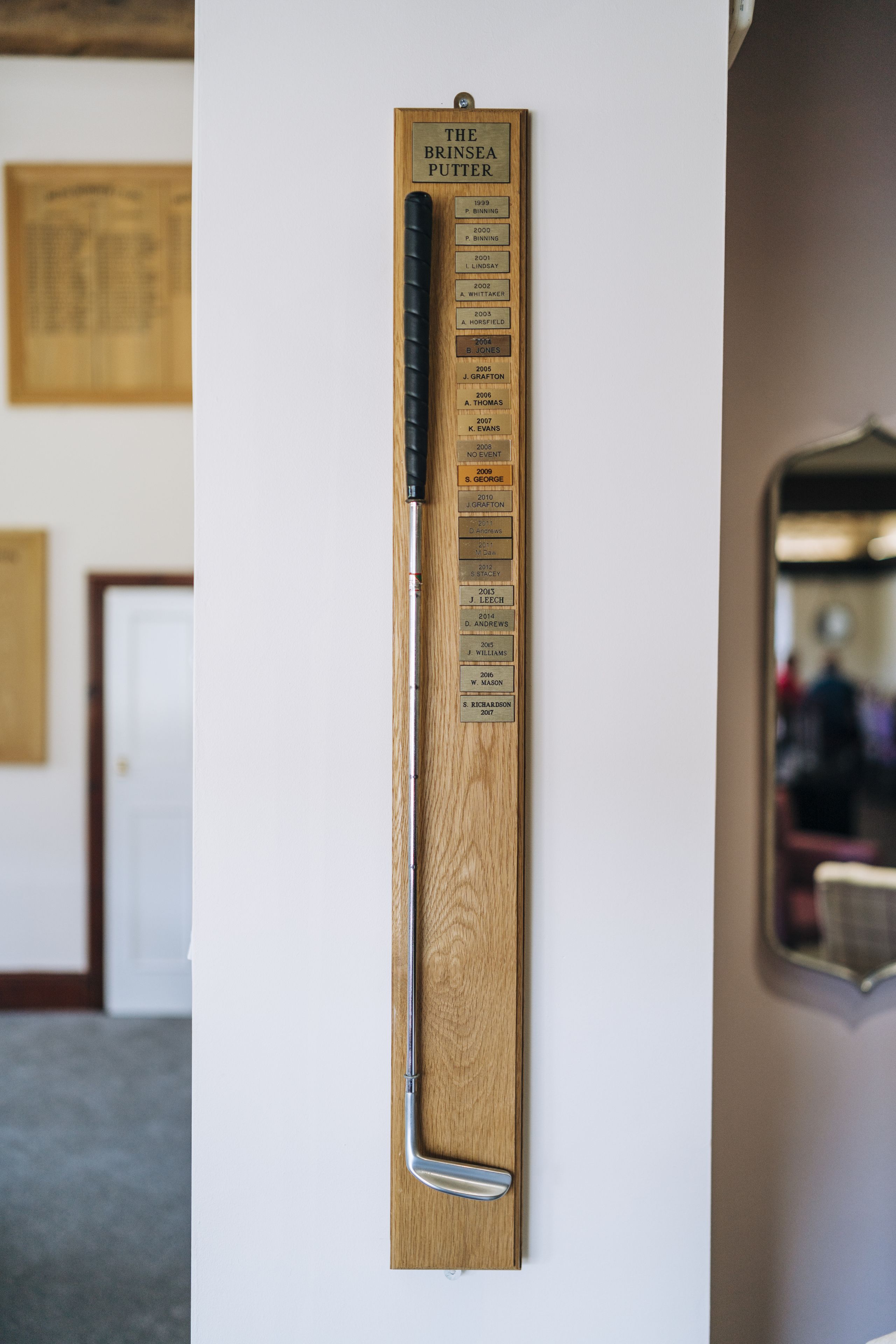 Een houten plaquette met een lijst namen en jaartallen, bevestigd aan een muur.