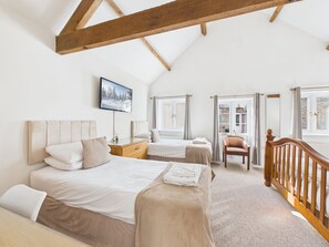 A bedroom with two beds, a wooden ceiling beam, a television, and a view of the outside. - Mendip Spring Golf Club (Bristol)
