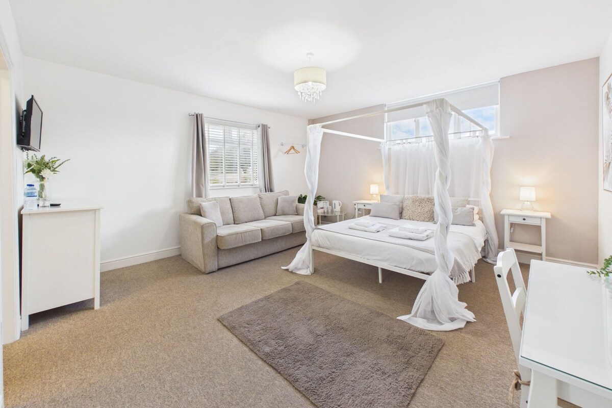 A bedroom with a four-poster bed, a sofa, a bedside table, a desk, and a chair.
