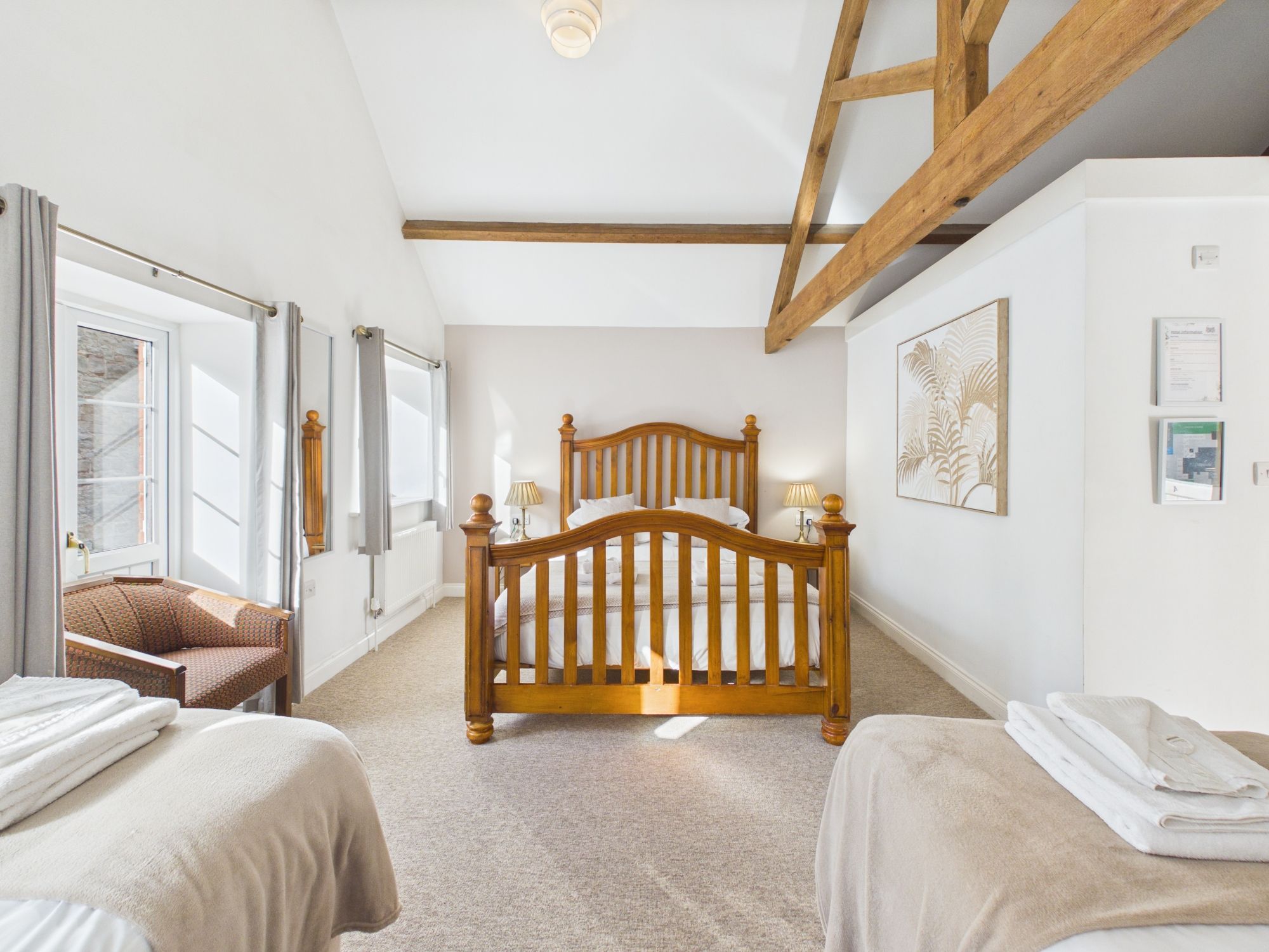 A bedroom with a wooden bed, two bedside tables, a chair, and a window with curtains.