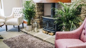 A cozy living room with a stone fireplace, two potted plants, and a tufted armchair. - Mendip Spring Golf Club (Bristol)