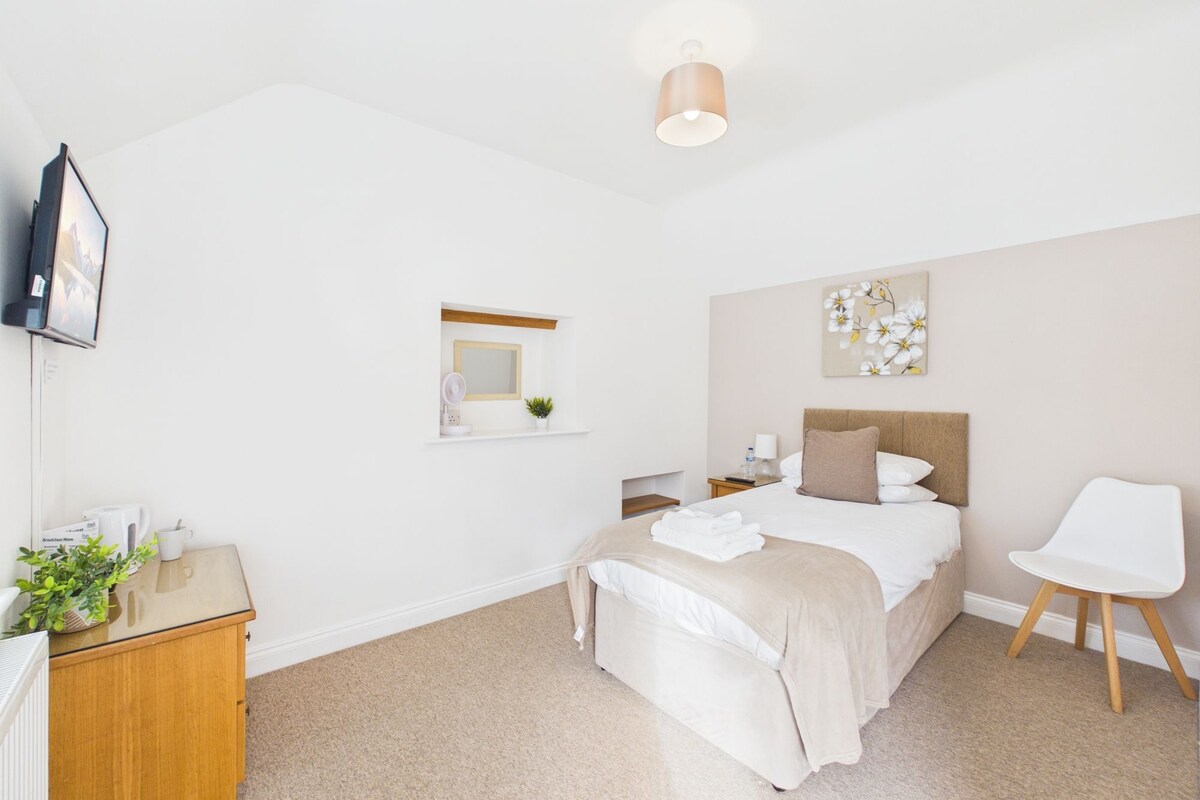 A hotel room with a bed, bedside table, chair, and a TV mounted on the wall.