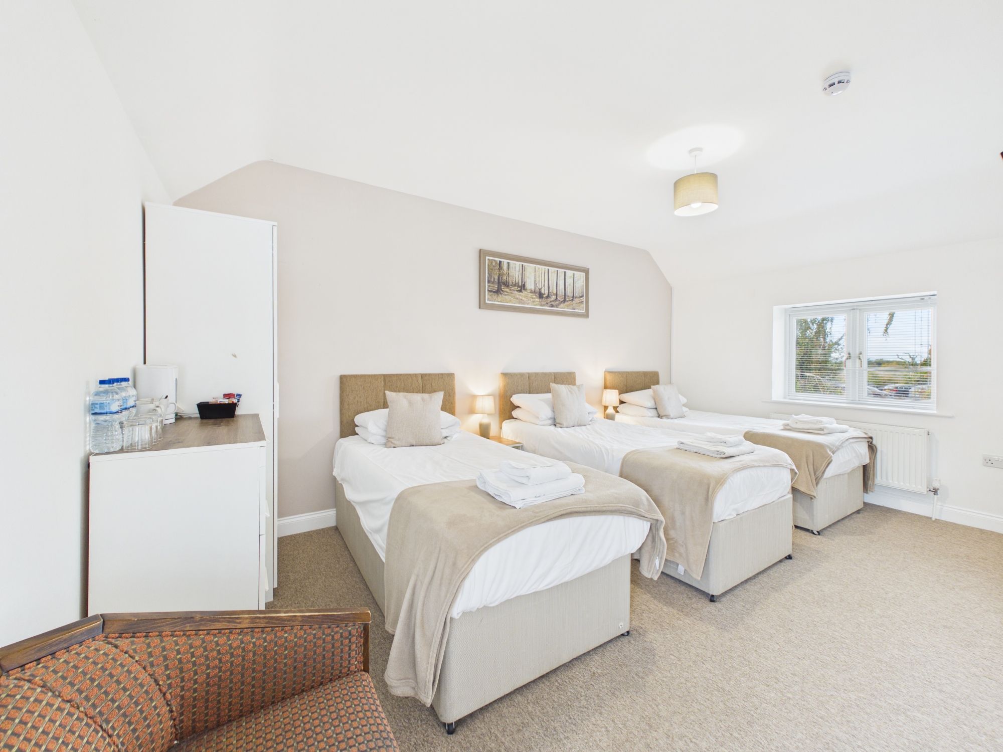 A hotel room with two beds, a desk, a chair, a window, and a painting on the wall.