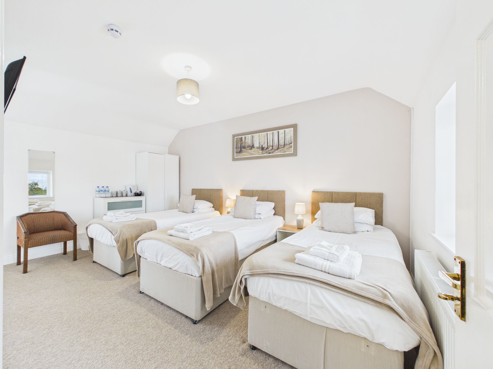A hotel room with three beds, a sitting area, a radiator, and a painting on the wall.